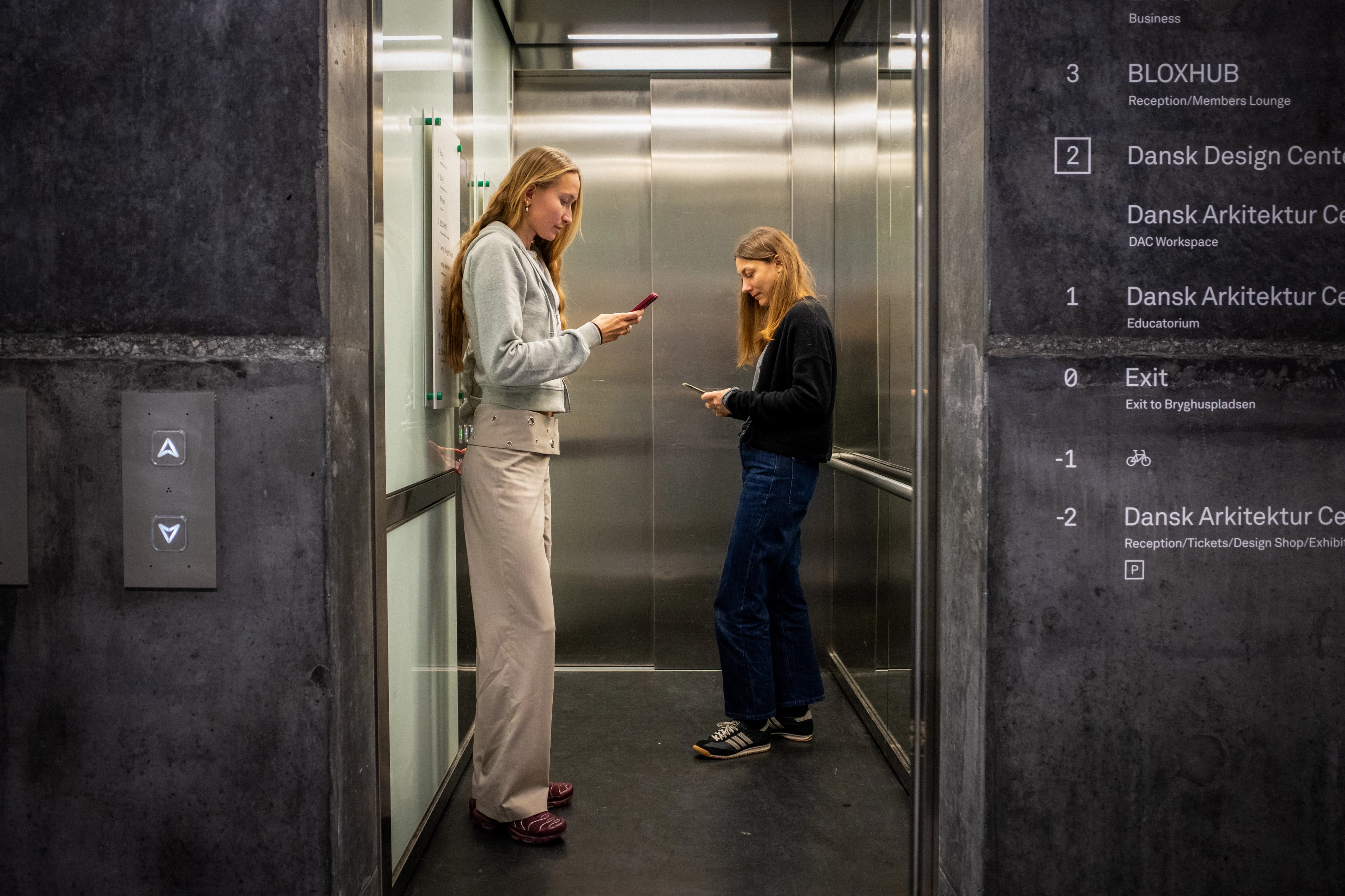 Elevator med to personer der kigger på deres telefon